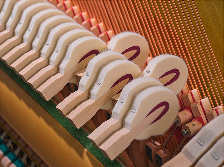 Close-up of piano action showing felt hammers aligned beside the strings inside a piano.