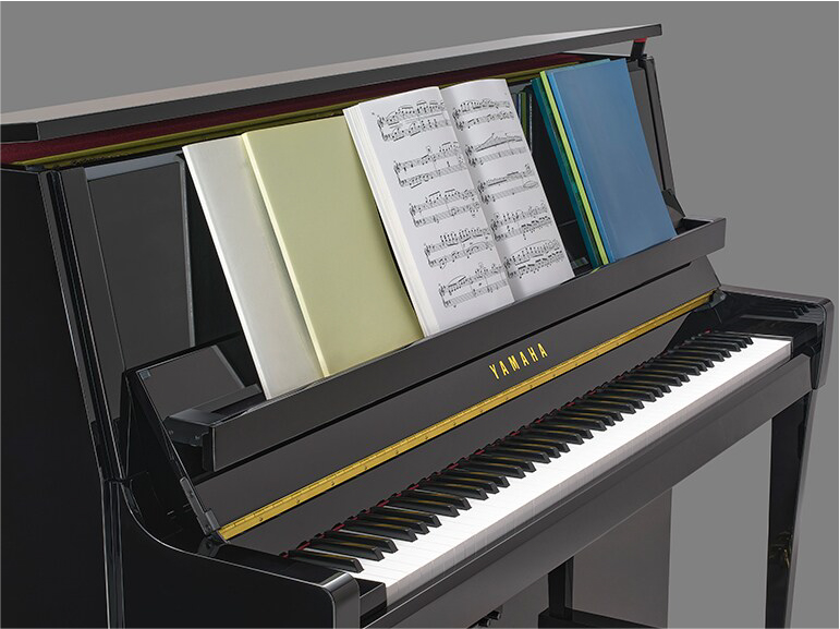 Yamaha upright piano with its lid open and sheet music on the music stand in front of the keyboard.