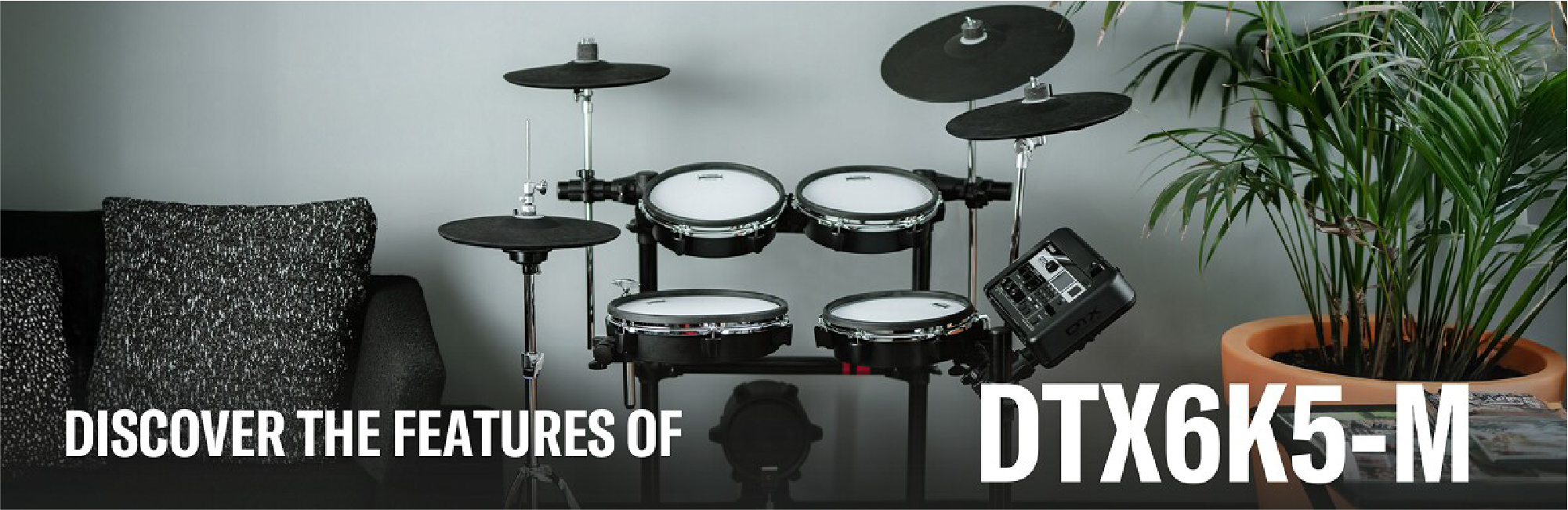 Electronic drum kit set up in a living room with a sofa and plant, featuring bold product text on the right (DTX6K5-M).