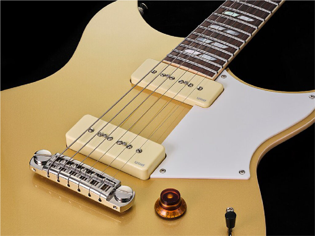 Close-up of a gold electric guitar body with a white pickguard, two cream pickups, and a chrome bridge plate.