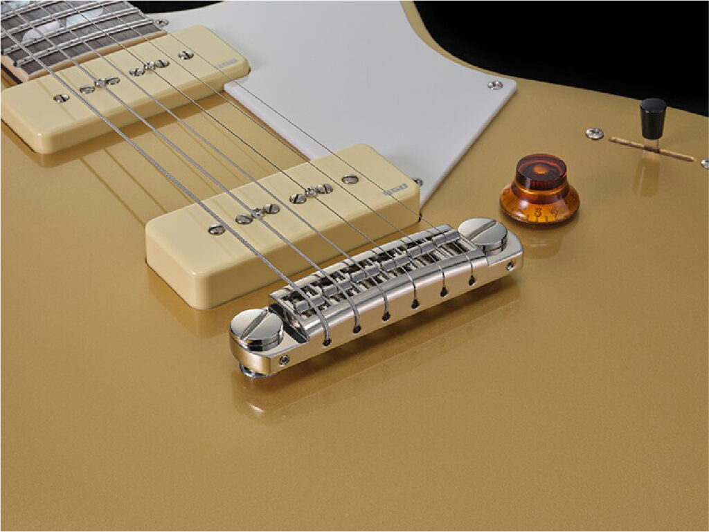 Close-up of a gold electric guitar showing the bridge, pickup covers, and control knob on a glossy body.