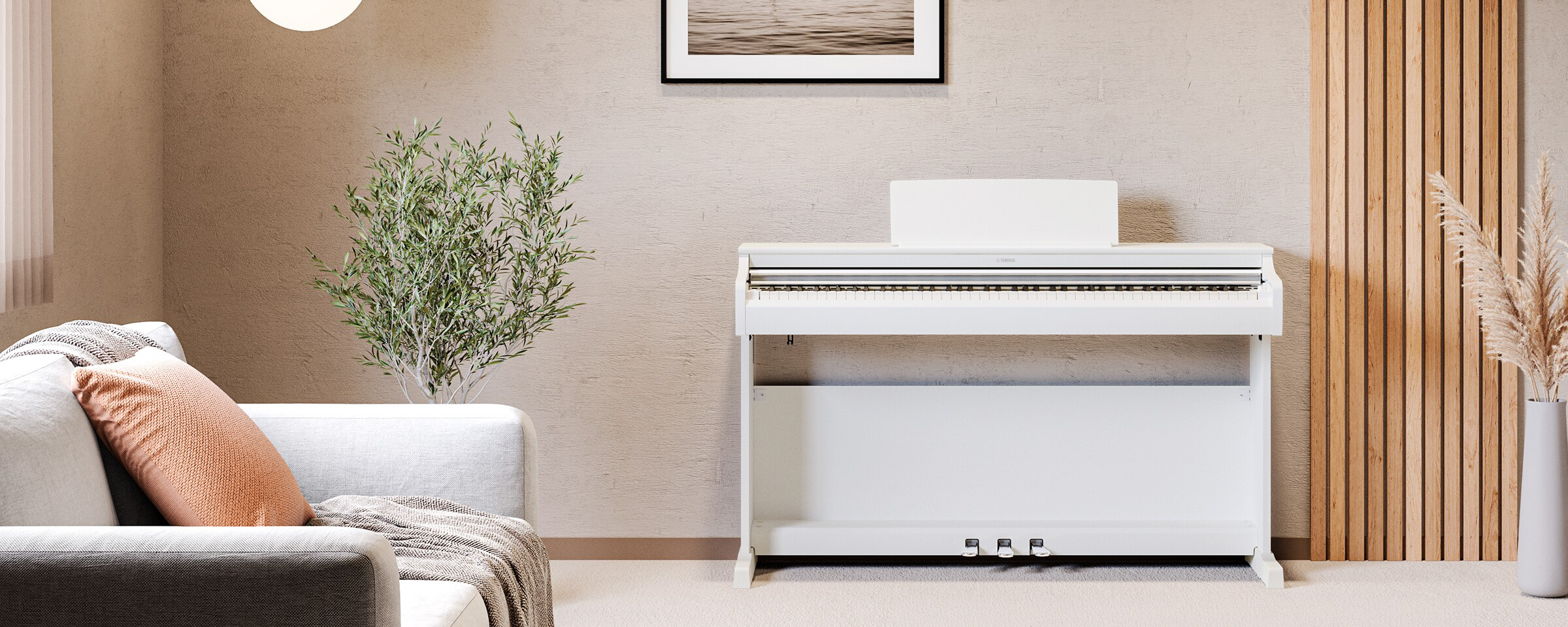 yamaha ydp-166r yamaha ydp-166wh 17 White upright piano against a beige wall in a cozy living room with a gray sofa, peach cushion, and tall green plant nearby.
