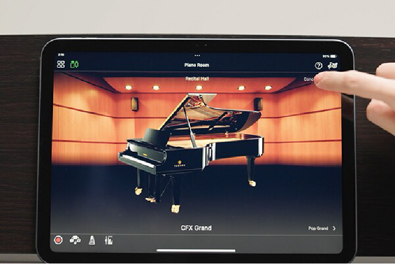 Tablet display showing a grand piano in a music app on stage, with a finger tapping the top-right area; text reads 'CFX Grand' on screen.