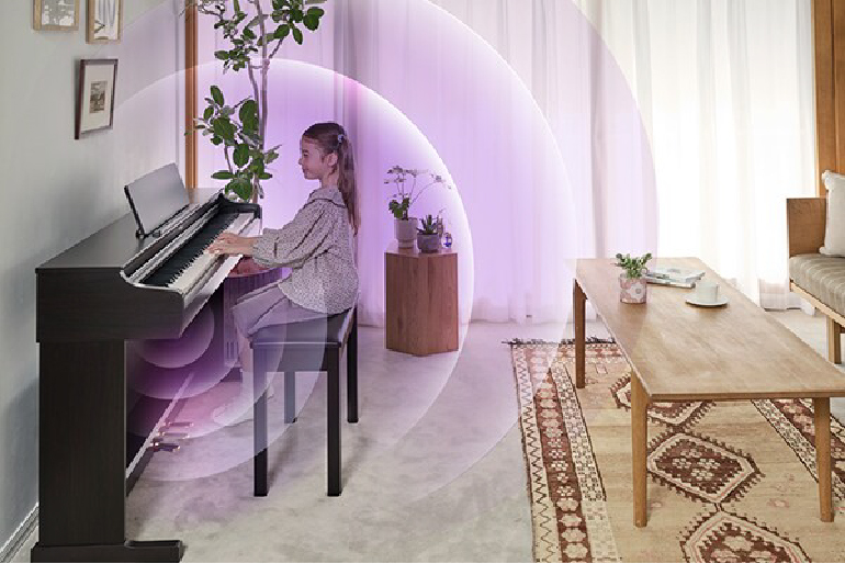 Girl sits at a dark upright piano in a bright living room with plants.