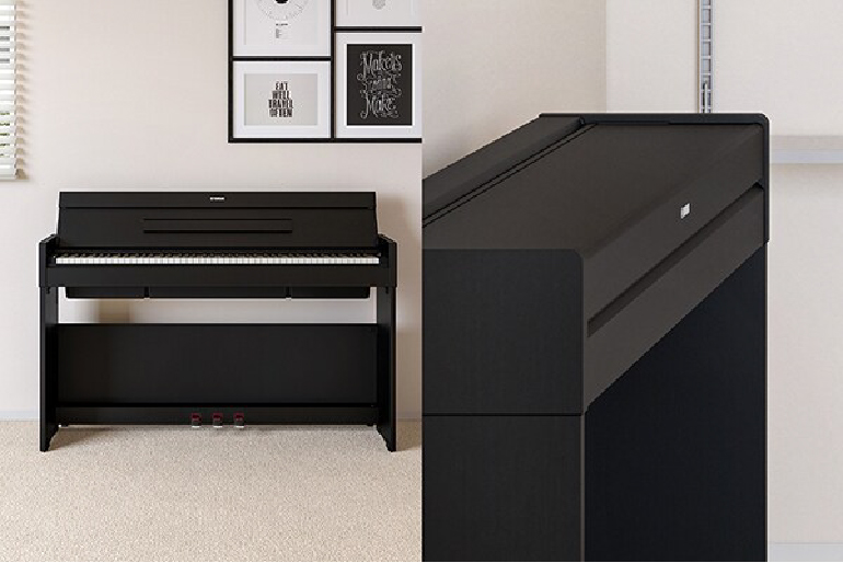 Black upright piano against a wall in a room, with framed art above it.