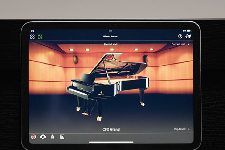 Tablet screen displaying a grand piano on a wooden recital hall stage in an app
