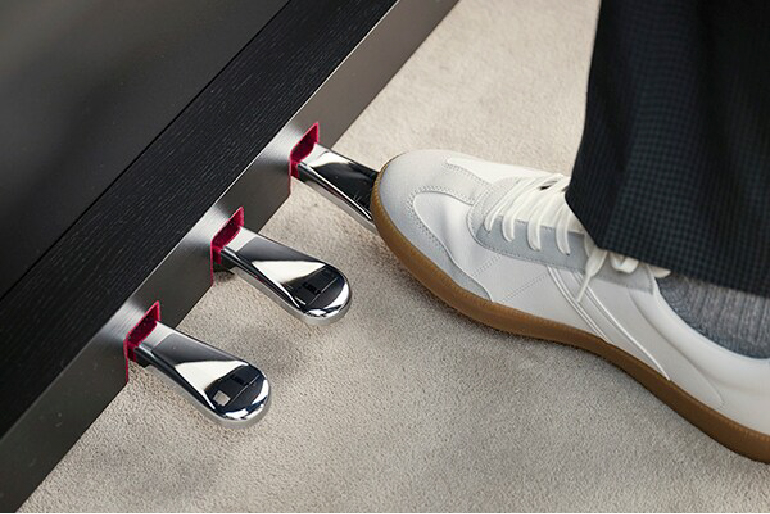 Close-up of a white sneaker pressing the right piano pedal with two other pedals visible behind it.