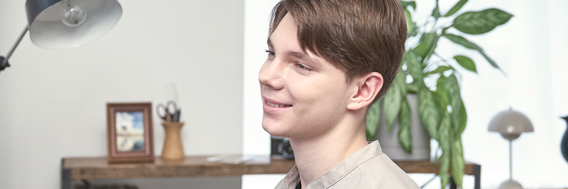 Yamaha YDP-S36B Profile view of a young man with brown hair smiling in a bright room, beige shirt, with a desk and plants in the background.