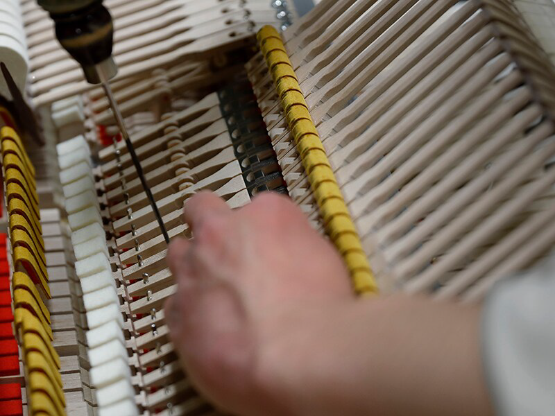 Piano technician tuning strings inside the piano with a tuning tool in hand (close-up).