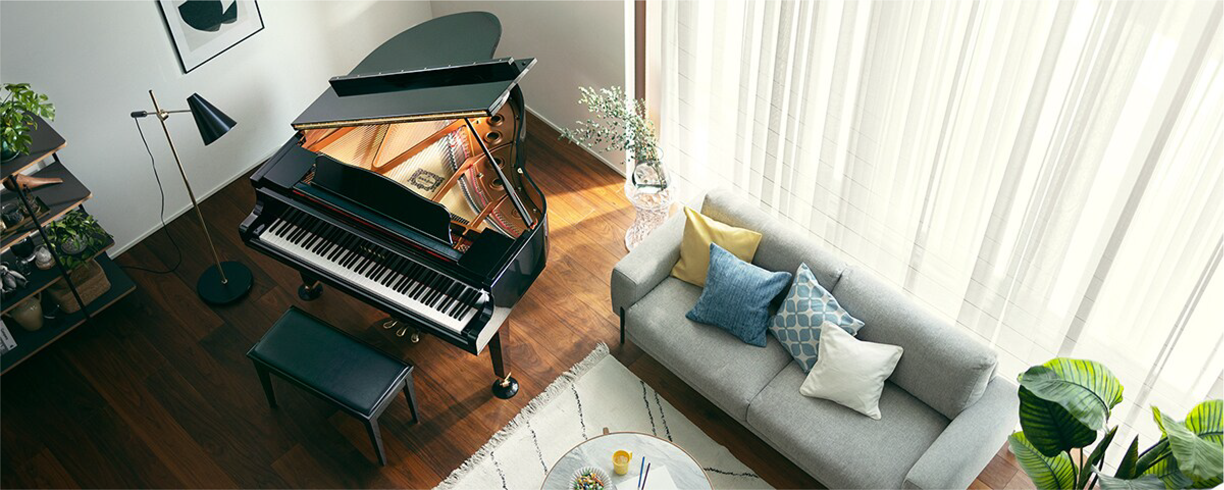 Open grand piano in a modern living room, with a gray sofa, colorful cushions, and sheer curtains by large windows.