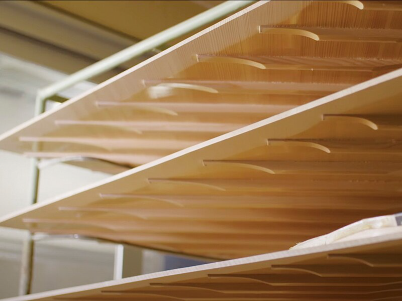 Close-up of light wood slats stacked in a workshop, each with curved ends, viewed from side.”,