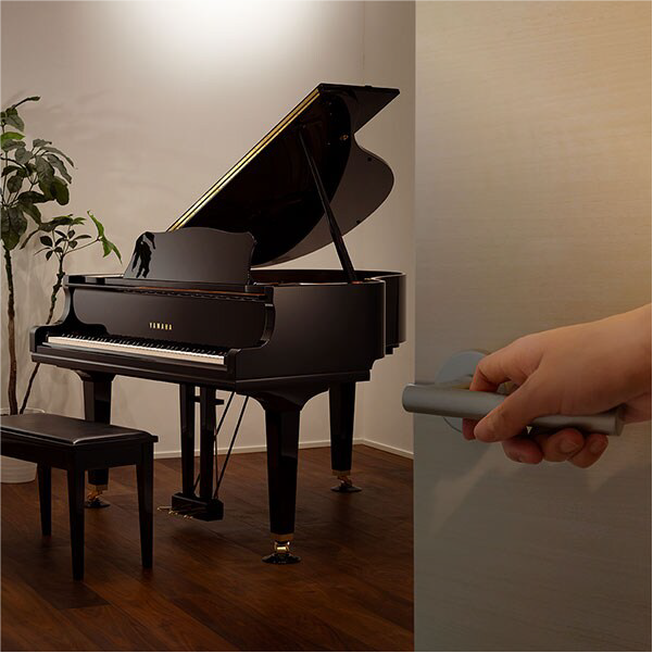 Grand piano in a room with a person holding a door handle near the doorway, foreground left to right.