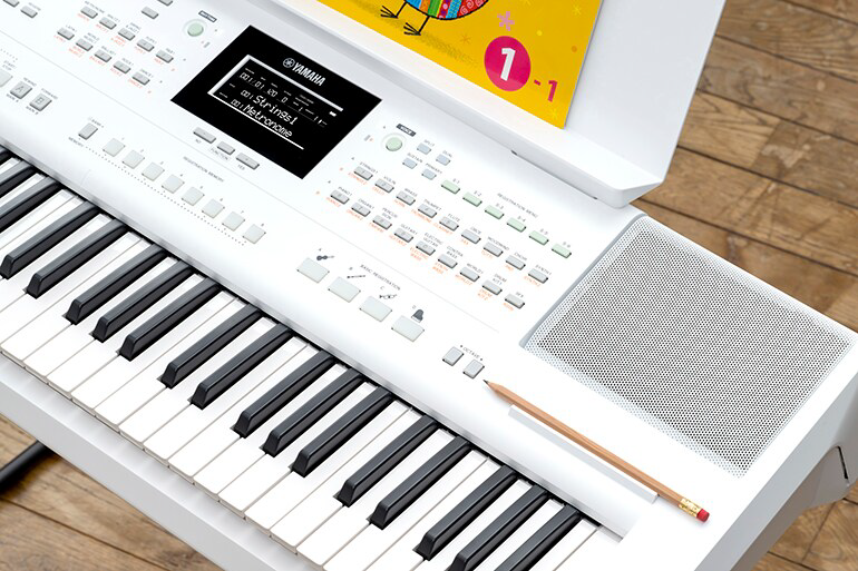 White Yamaha digital keyboard with a control panel and speakers, a wooden floor, and a pencil resting on the keys.