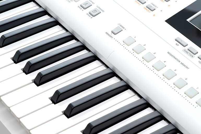 Close-up of black and white piano keys with part of a digital keyboard's control panel in the background