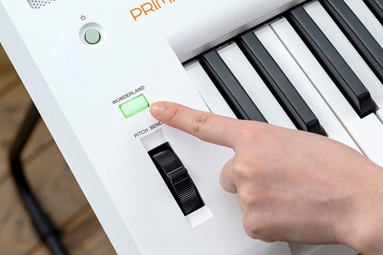 Hand presses a glowing green 'WONDERLAND' button on a white electronic keyboard/synthesizer panel visible with black-and-white keys nearby.