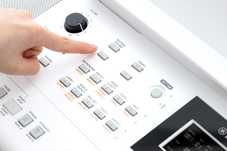 Close-up of a hand pressing a button on a white drum machine, with labeled tempo and rhythm controls visible.