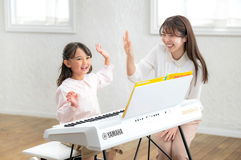 A young girl and a smiling woman give each other a high‑five while playing a Yamaha keyboard in a bright room.