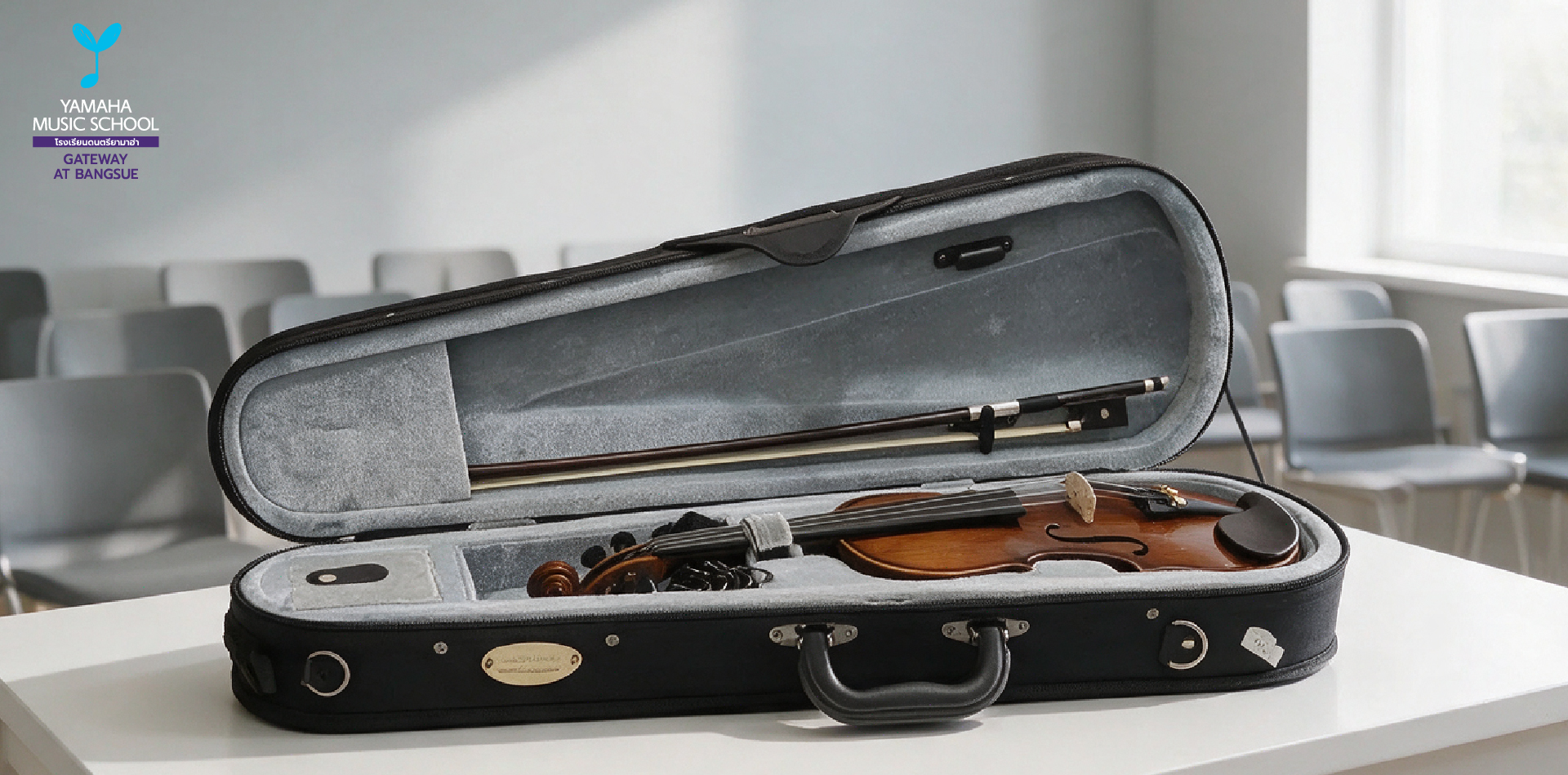 Open violin case on a white table in a classroom; violin and bow inside, Yamaha Music School logo in the top-left corner.