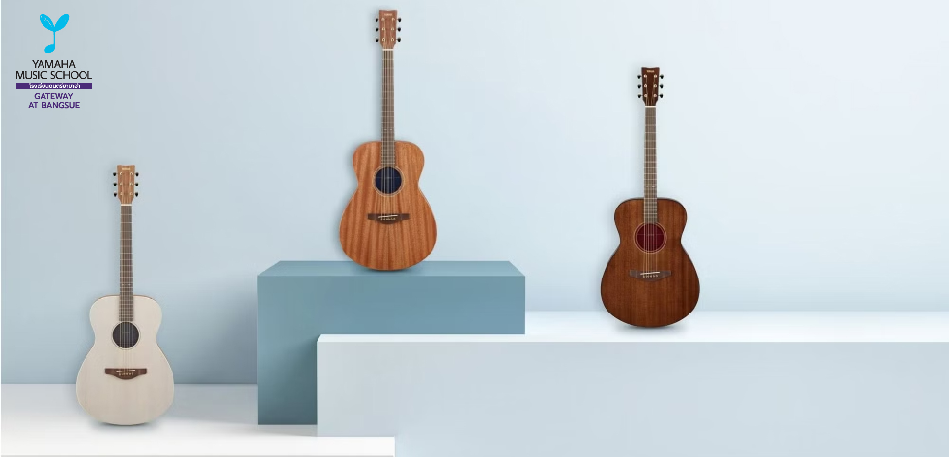 Three acoustic guitars on light blue geometric pedestals against a pale blue wall, with a Yamaha Music School logo in the top-left corner (Gateway at Bangsue).
